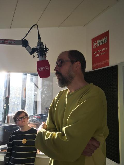 Rainer Garburg während der Aufnahme. Rainer spricht in ein Mikrofon, welches an einem Ständer von der Decke hängt.
